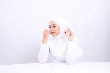 Çekici makyaj dudakları genç Asia duvak güzel zarif bir bakış kamera eli dudaklara ruj sürerken ve kapak izole beyaz arka plan. Kozmetik reklam konsepti, dudak rengi, ruj modeli