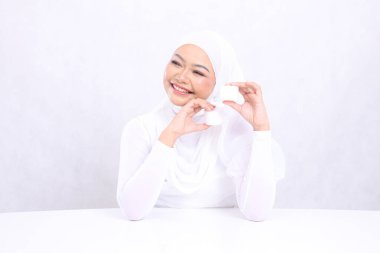 Güzel genç tesettürlü kadın beyaz arka planda günlük cilt bakımı gereksinimleri için kozmetik kremi üst tabanı tutarak mutlu oldu. Yüz bakımı, mükemmel cilt.