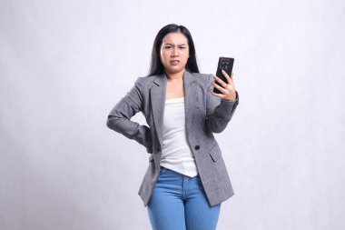 Güzel, yetişkin ofis hanımları Asia kameradan tiksinmiş, cep telefonu tutan, beyaz arka planda izole edilmiş gri takım elbiseli. teknoloji, yaşam tarzı, alışveriş, işlem içeriği