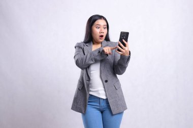 Güzel, genç bir ofis kadını, cep telefonuna dokunurken şok oldu. Beyaz arka planda gri takım elbise giyiyordu. teknoloji, yaşam tarzı, alışveriş, işlem içeriği