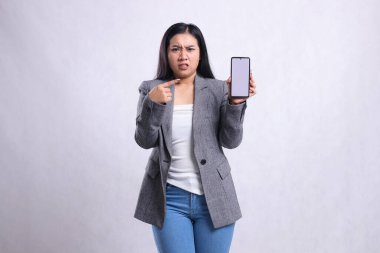 Güzel, olgun ofis kadını Asia, kameraya kızgın ve beyaz arka planda izole edilmiş gri takım elbise giyen cep telefonu ekranını gösteren bir jest yaptı. Teknoloji, yaşam tarzı ve tanıtım içeriği için