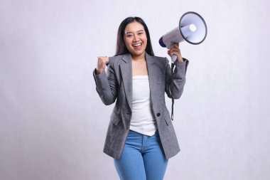 Güzel, yetişkin bir kadın, megafon hoparlörünü tutan ve beyaz arka planda izole edilmiş gri takım elbise giymiş, neşeli bir şekilde el ele bağırıyor. moda konsepti, duyuru