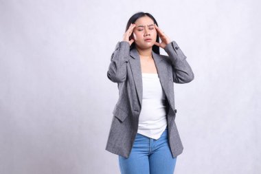 expression of beautiful young office woman asia close eyes dizzy both hands hold head tilted left wearing gray suit standing isolated on white background. for health, medical, commercial, prevention clipart