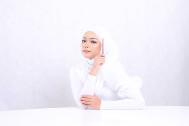 Endonezya 'nın yetişkin kadın tesettüre alımlı makyajı kamera eline kaş kalemi yanında beyaz arka planda izole edilmiş temiz, parlak bir cilde sahip. Kozmetik reklamcılık, kaş kalemi maketi