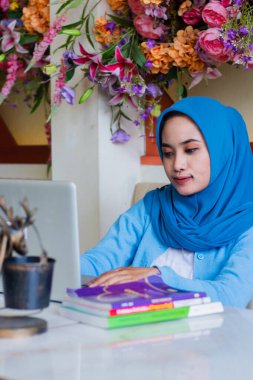 Başörtüsü takmış güzel Asyalı bir kızın portresi dizüstü bilgisayarında yazarken gülümseyen kahve dükkanındaki bir masada ödevlerini yapan. İletişim içeriği, reklamcılık, yaşam tarzı, teknoloji için