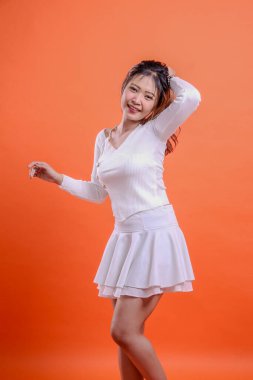 Beyaz bluzlu, güzel bir Asyalı kadın model. Geniş, neşeli, geniş, sağa eğimli. Saçlarını arkada tutuyor ve izole edilmiş turuncu arka planda dans ediyor. moda konsepti, reklam, promosyon, reklam