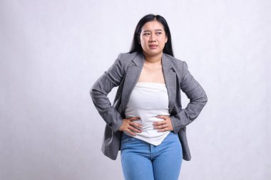 gesture beautiful cheerful young woman indonesia frowning candid stomachache wearing grey suit and jeans standing isolated on white background. for health, treatment, commercial, prevention content clipart