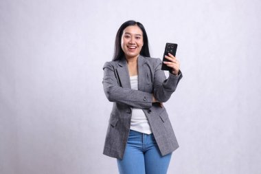Güzel ofis hanımlarının portresi kameraya neşeli ve beyaz arka planda izole edilmiş gri takım elbiseli cep telefonlu Asya. teknoloji, yaşam tarzı, alışveriş, işlem içeriği