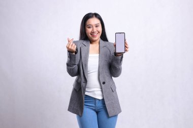 Beyaz arka planda izole edilmiş gri bir takım elbise giyen, cep telefonu ekranını gösteren, sevgi dolu, genç ve güzel ofis kızı ifadesi. Teknoloji, yaşam tarzı, promosyon