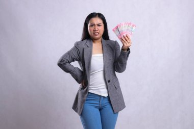 Beyaz arka planda izole edilmiş gri takım elbise giyen ve Rupiah 'ın parasını tutan kızgın bir ofis kadınının ifadesi. hediye içeriği, yaşam tarzı, ödül, etkinlik, yarışma