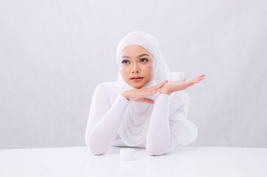 Güzel genç bayan tesettür zarif görünüyor sol üstte kozmetik krem tutuyor ve cilt bakımı için avuç içi çekiyor ana ürün tanıtımı için izole edilmiş beyaz arka plan. Sağlık, sağlık ve moda kavramı