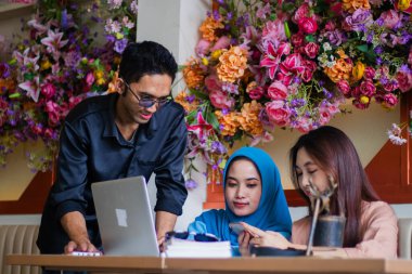 Bir grup Asyalı serbest çalışan cep telefonuyla kahve dükkanındaki bir şirketin dizüstü bilgisayarının önünde sunum dinliyorlar. grup konsepti, şirket, eğitim, eğitim, iş