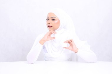 Güzel genç başörtüsü kadın kameraya odaklanıyor. Her iki el de beyaz arka planda günlük cilt bakımı gereksinimleri için kozmetik kremi tutuyor. Yüz bakımı, doğal makyaj.
