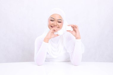 Güzel, neşeli genç tesettürlü kadın beyaz arka planda günlük cilt bakımı için iki elinde kozmetik krem tutan kreme bak. Yüz bakımı, mükemmel cilt.