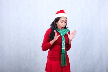 Noel Baba şapkası ve eşarpla kırmızı süveter giyen kız ifadesi Noel ve yeni yılı kutluyor, iki elini de kaldırıyor kusmak istiyor, beyaz arka planda izole edilmiş.