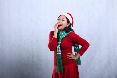 Noel Baba şapkası ve eşarbıyla kırmızı süveter giyen portre kadın, kameraya mutlu bir şekilde gülüyor, belini tutuyor ve ağzını kapatıyor, beyaz arka planda yeni yılı ve Noel 'i kutluyor.