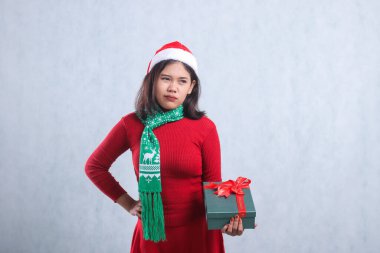 Asian beauty ladies wearing christmas sweater, Santa hat and scarf, thinking about something hand holding green merry christmas gift box and waist, isolated on white background clipart