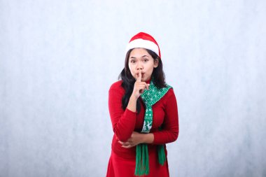 portrait woman expression wearing red sweater party wear with Santa hat and scarf celebrating christmas and new year, arms folded signifying silence do not make noise, isolated on white background clipart