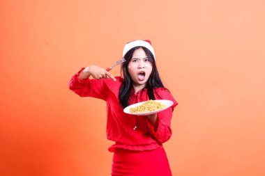 Yetişkin bir kadın kameraya bakarken şaşırdı. Elinde çatal, elinde erişteyle dolu beyaz tabak vardı. Kırmızı Noel bluzu, Noel Baba şapkası giyiyordu.