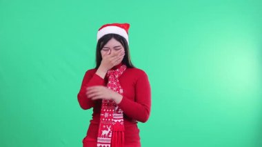 Noel süveteri, Noel Baba şapkası ve eşarbı giyen kadınlar osuruk kokusu alırken yeşil arka planda işaret eden birini suçlarlar..