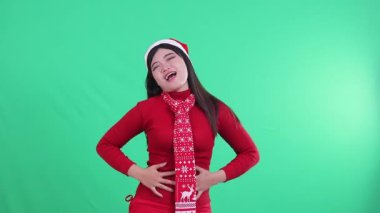 Asyalı kadın dışkıladıktan sonra mutlu ve rahatlamış görünüyor, Noel süveteri giyiyor, yeşil arka planda Noel Baba şapkası ve eşarp takıyor, yeşil ekran.
