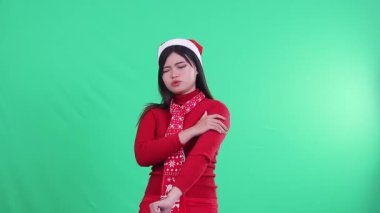 Noel kazağı giyen kız, Noel Baba şapkası ve eşarbı takan, yaralı kolu tutarken acı gösteren ya da yeşil ekran arka planında kaslarını çeken kız..
