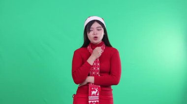 Genç Asyalı kadın Noel süveteri giyiyor, Noel Baba şapkası ve atkı takıyor. Hasta bir yüz ifadesi var, hapşırıyor, bir elinde beyaz doku, izole edilmiş yeşil arka plan, yeşil ekran.
