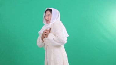 Beyaz tesettürlü ve beyaz elbiseli Müslüman bir kadın göğsünü tutuyor. O, yüzü görünür bir yan görünüm ile görülmektedir. Arkaplan izole edilmiş yeşil arkaplan veya yeşil ekran.