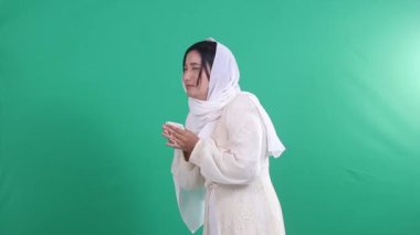 Beyaz tesettürlü genç bir kadın hapşırdığı için hasta, elleri mendille kaplı. İzole edilmiş yeşil arkaplan veya yeşil ekran.