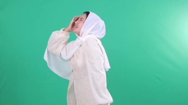 Beyaz elbiseli ve tesettürlü bir kadın. Başında acı ve acı dolu bir ifade, kollarını kavuşturup başını yeşil bir zeminde ya da izole edilmiş yeşil bir ekranda tutuyor..