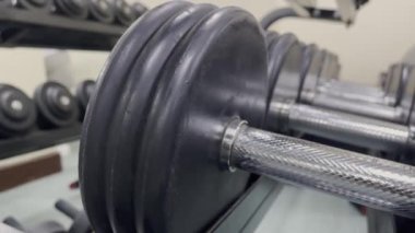 Görüntü, spor salonundaki birkaç dambılın yakın çekimini gösteriyor, ağırlıklar siyah ve gümüş renkte, antrenman veya antrenman için hazır. Spor ve eğitimi betimliyor..