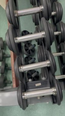 Spor salonunda ağırlık kaldırma ve karın gereçleri. Siyah ve gümüş metalden yapılmış ağırlıklar bir rafta oturur. Odada açık yeşil döşeme var..
