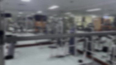Bu, çeşitli fitness ekipmanlarının yer aldığı bir jimnastik salonunun bulanık görüntüsü. Resim çeşitli makine ve diğer egzersiz araçları ile odak dışı bir arkaplan sağlar.