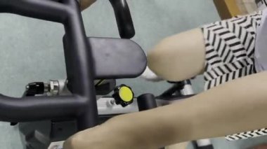 Kapalı devre bisiklet makinesinin siyah gidonunu tutan bir insanın ellerini kapatın, ekipmana ve kişinin bacaklarına odaklanın..