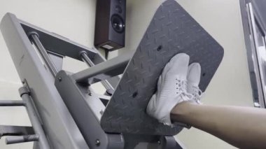 Bu bir bacak pres makinesinin yakın çekim görüntüsü, beyaz ayakkabılar giyen bacak platformda, antrenman için hazır..