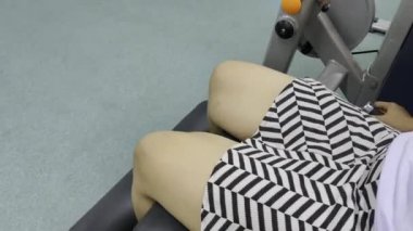 Bir insanın bacaklarına yakın çekim, desenli bir etekle, siyah bir pedin üzerinde oturarak ve spor salonunda bacak egzersizi yaparak, fiziksel sağlık için egzersiz yaparak..