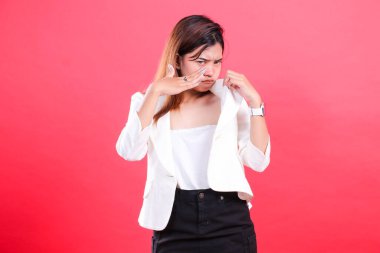 Beyaz ceketli ve siyah pantolonlu bir kadın ceketini ayarlıyor ve kırmızı arka planda izole bir şekilde kameranın önünde poz veriyor.