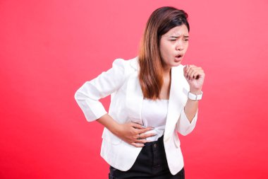 Karnını tutarken beyaz ceketli bir kadın öksürüyor. Bu görüntü, kırmızı bir arka planda izole edilmiş, rahatsız bir şekilde öksüren bir kişinin görüntüsü..