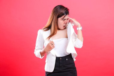 Beyaz ceketli ve siyah pantolonlu bir kadın gömleğini burnundan uzak tutuyor. Yüzünde iğrenç bir ifade var. Kırmızı arka planda izole edilmiş.