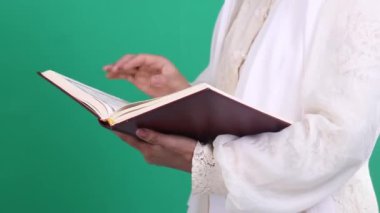 Beyaz lacey kollu bir kişi açık bir kitap olan Kuran 'ı elinde tutuyor, Arapça yazılı ve kırmızı kapaklı, yeşil arka planda veya yeşil ekranda izole edilmiş..