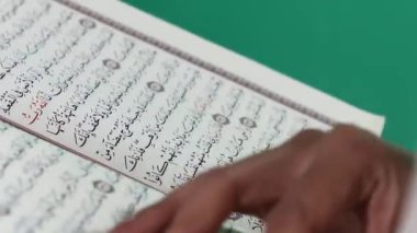 Bir el, Kuran 'ın Arapça reçeteli bir sayfasına işaret ediyor, İslami kutsal kitap, kelimelere odaklanmış, yeşil arkaplanda ya da yeşil ekranda izole edilmiş..