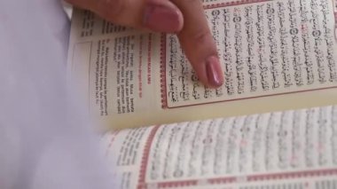 Açık Kur 'an' a pembe ojeli bir kişinin eli, sayfalarda görünen Arapça metin, yeşil arkaplanda ya da yeşil ekranda izole edilmiş..