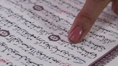 Yakın plan çekimde bir kişinin parmağı, Arapça bir metni işaret ediyor. Bir kitapta, muhtemelen Kuran 'da. yeşil arkaplanda ya da yeşil ekranda izole edilmiş