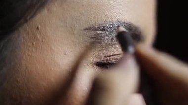 Kaşlarını kalemle şekillendiren bir kadının yakın çekimi. Yüz geliştirme için güzellik, makyaj ve kozmetik prosedürlerine odaklanın.