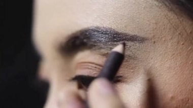 Kaşlarını kalemle şekillendiren bir kadının yakın çekimi. Güzellik süreci, kozmetik tedavi ve kaş tasarımı ayrıntıları..