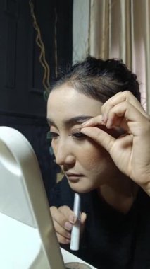 Bir kadın dikkatlice takma kirpiklerini takıyor, bir olaya hazırlanıyor. Kendi makyajını yapıyor, aynaya bakıyor, içeride..