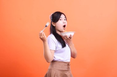 Ağzı açık neşeli genç bir kadın elinde çatalla turuncu arka planda izole bir şekilde şehriye yer..