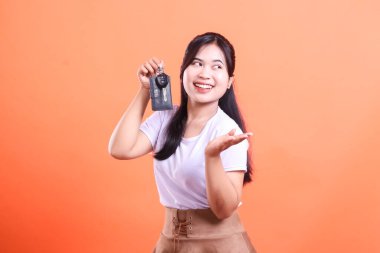 Heyecanlı Asyalı kadın yeni araba anahtarlarını büyük bir gülümsemeyle gösteriyor. Yan tarafa bakıyor ve sunum yapıyor. turuncu arkaplanda izole