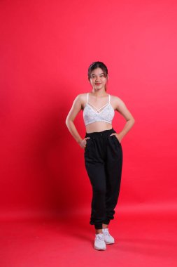 Spor sutyen ve eşofman giyen bir kadın elleri cebinde duruyor. kırmızı arkaplanda izole edilmiş