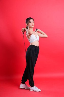 Beyaz bluzlu ve siyah pantolonlu bir kadın siyah bir ip tutuyor, kameradan uzağa bakıyor, kırmızı bir arka planda izole edilmiş..